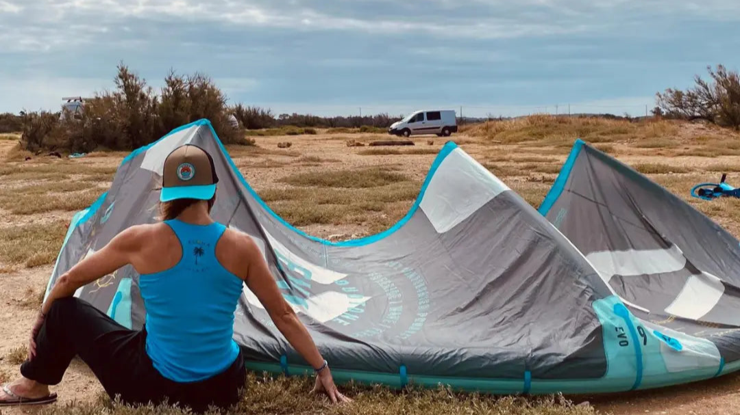 Image d'un débardeur femme surfwear  bleu turquoise avec  un logo palmier dans le dos à coté d'une aile de kitesurf de la marque Alohasurfwear