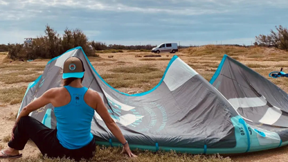 Image d'un débardeur femme surfwear  bleu turquoise avec  un logo palmier dans le dos à coté d'une aile de kitesurf de la marque Alohasurfwear